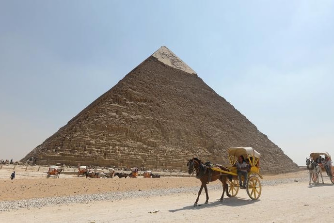 Horse and carts travel in front of a large pyramid