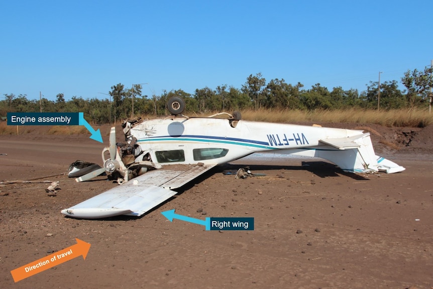 A photo of a small plane which has crashed and lies upside down on a road. A number of things have been pointed out with arrows