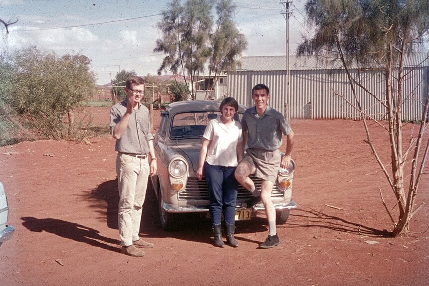 Three people stand in front of car in the outback