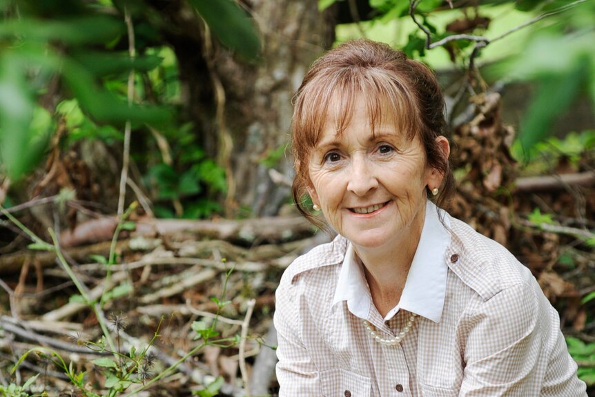 A woman with red hair, in a white business shirt, sitting in the forest.