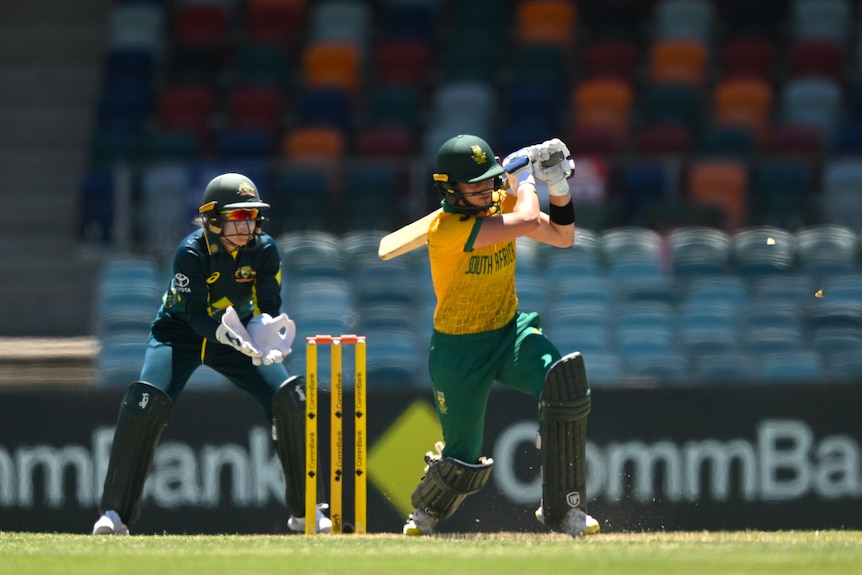 Laura Wolvaardt, in a gold shirt, hits to the leg side in front of Australian wicketkeeper Alyssa Healy.