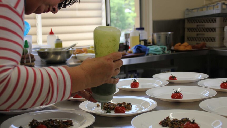 Amanda adds a green sauce to plates bearing tomatoes and some grilled vegetables.