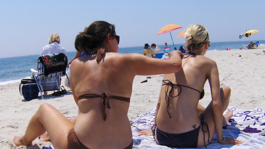 A woman applying sunscreen to another woman's back on the beach