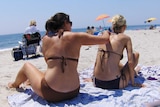 A woman applying sunscreen to another woman's back on the beach