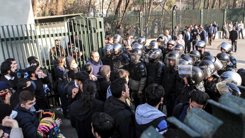 A group of protestors faces off against armoured police.