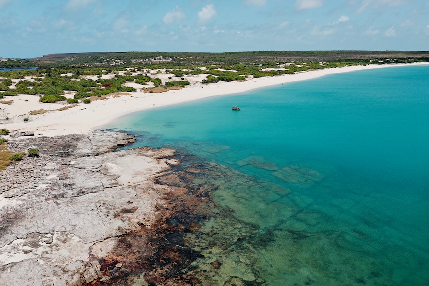 An aerial view of ocean, sand and rock formations on the coastline of an island.