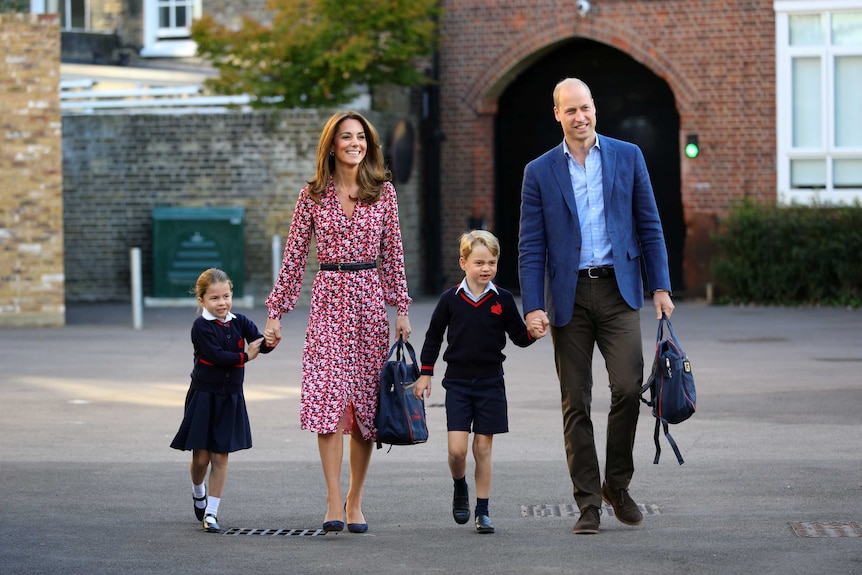 The Duke and Duchess of Cambridge carry walk with their two young children in school uniform along an empty driveway.