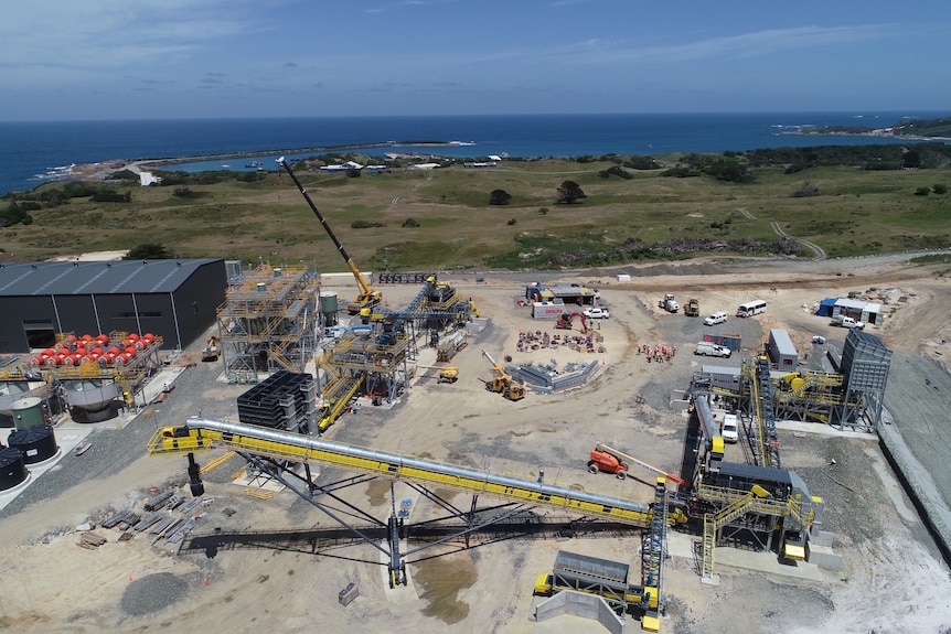 An aerial view of construction workers and equipment with the ocean in the background.