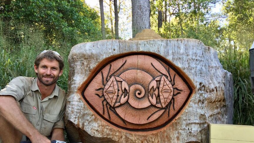 A man sits next to a large wood carving