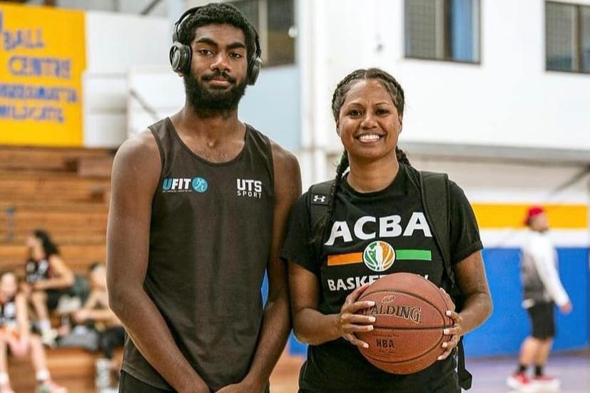 Buru and his sister Josie at a basketball court. Josie is holding a basketball. Buru has headphones on.