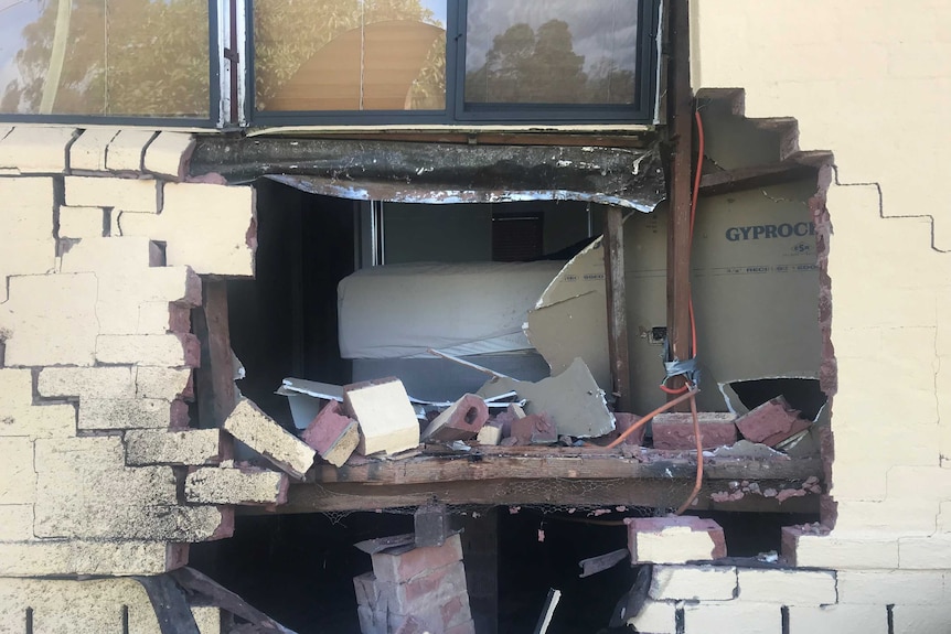 A bed is visible through a hole in the front of a house.