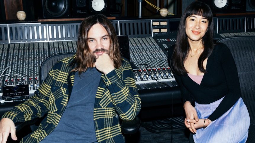 Kevin Parker (black and white patterned shirt) and Linda Marigliano (black shirt, blue skirt) sit in a recording studio