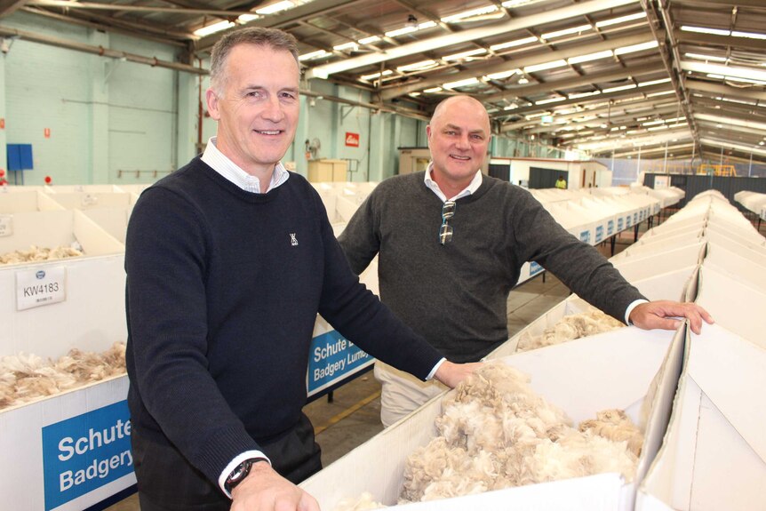 Two men in jumpers stands with lots of tubs of wool