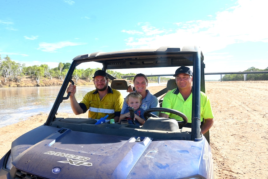 Two men, a woman and a small child sit in a farmer's utility vehicle in the middle of the Gascoyne River bed with some water.