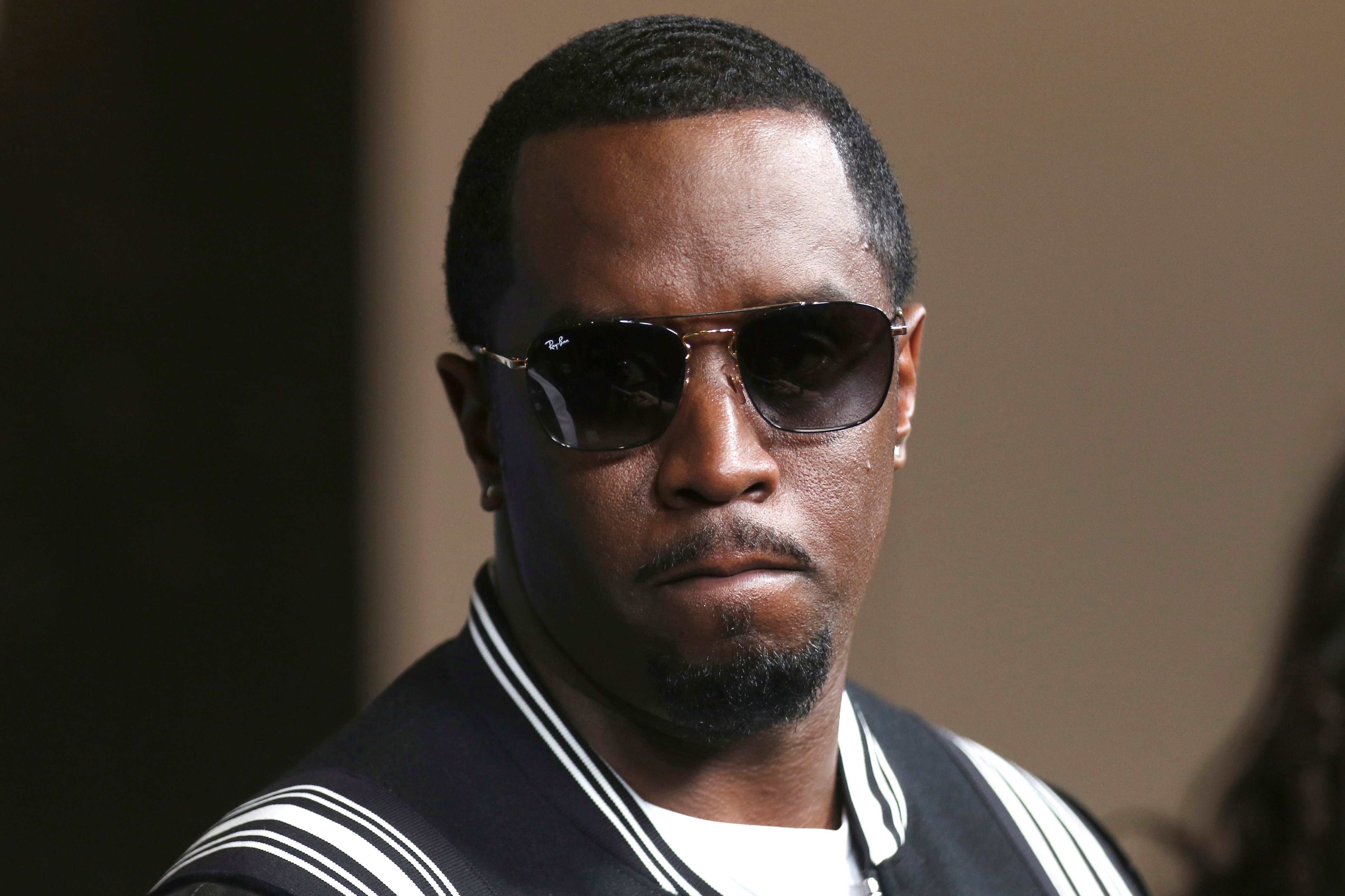 A headshot of Sean Combs wearing sunglasses and a black and white striped jacket