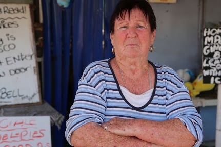 A woman stands outside a shop with her arms folded.