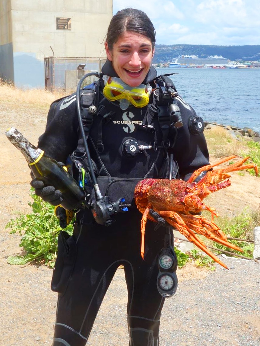 Woman in scuba gear poses with wine bottle and crayfish after dive in River Derwent.