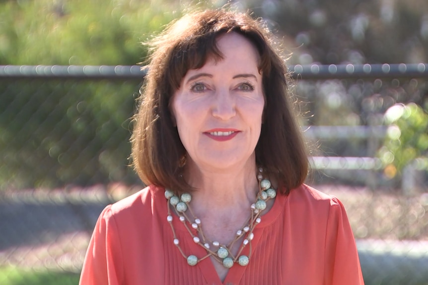 a woman in an oraange top looking at camera  head and shoulders view 