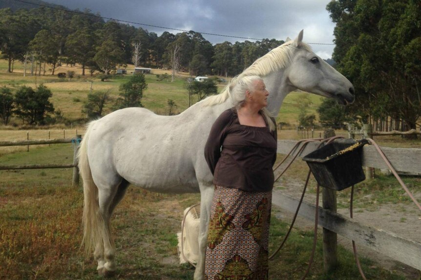 Woman in the countryside, standing with a white horse. They're both looking away in the same direction.