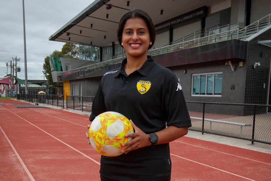  Aish Ravi holds a soccer ball while standing on an atheltics track.