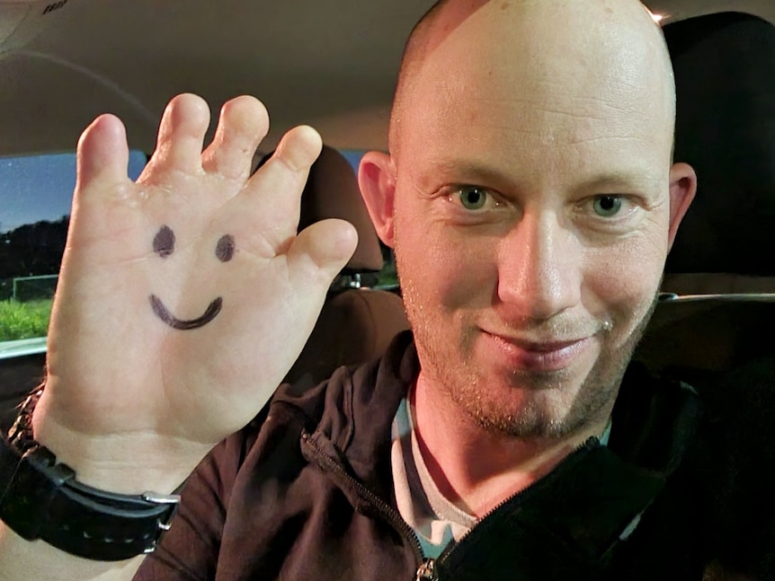 Stuart John holds up a hand with a smiley face drawn on it.