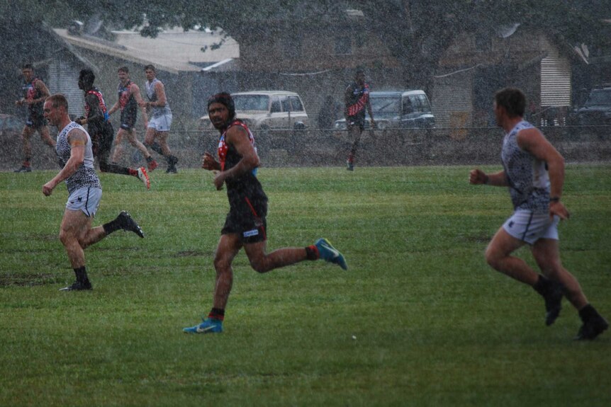 Cyril Rioli runs through the rain. There is a Palmerston player on either side of him.