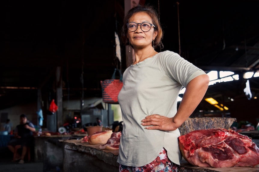 A woman stands with her hand on her hip, next to a table with raw meat