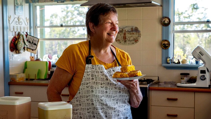 Woman in kitchen holds plate of scones.