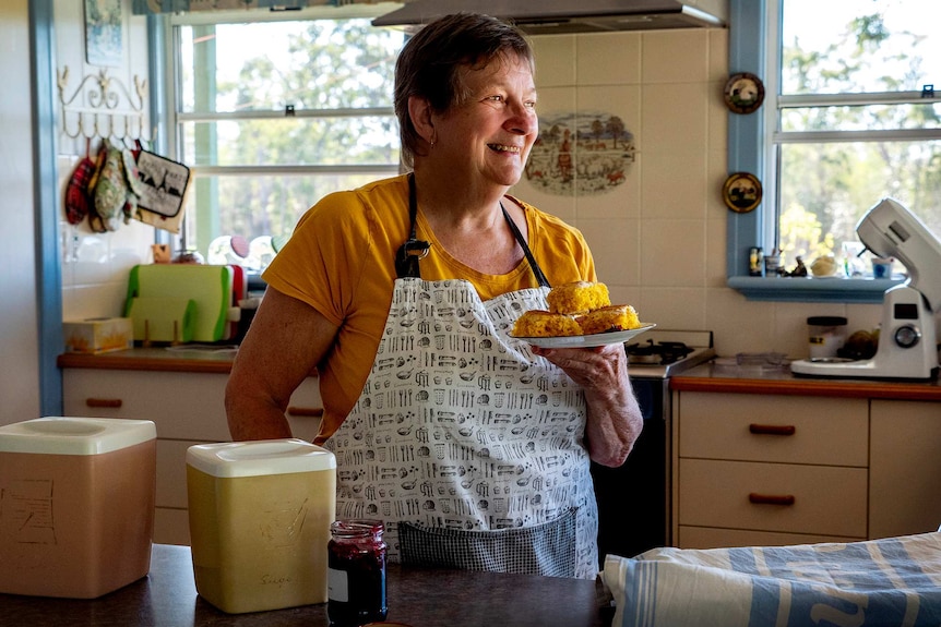 Woman in kitchen holds plate of scones.