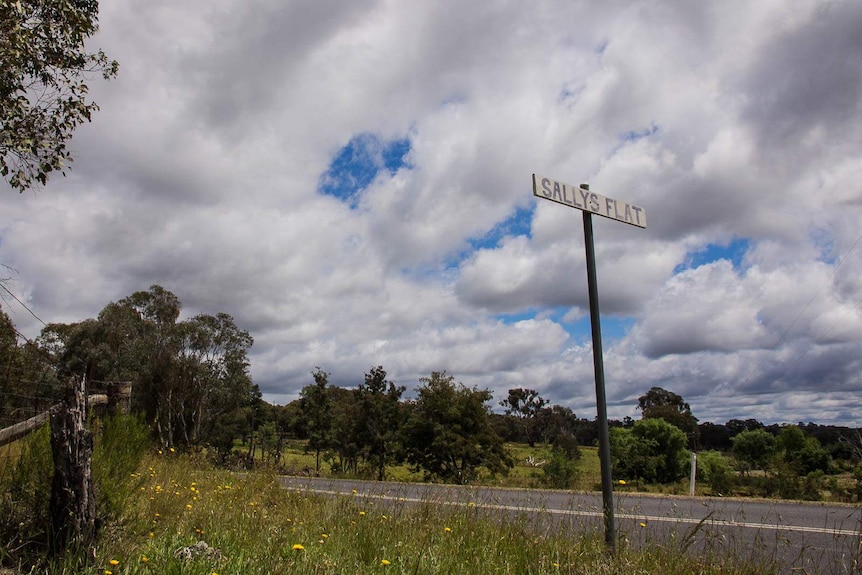 Sign saying Sallys Flat on a country road with farmland in the background
