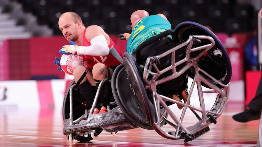 Denmark wheelchair rugby player tucks the ball away from Australian Ryley Batt tipping his chair onto him