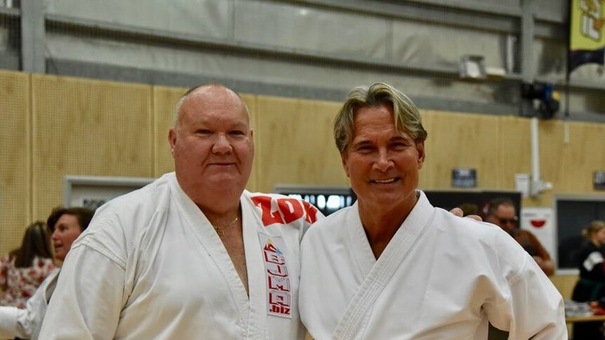 Two men standing in martial arts clothes smiling.