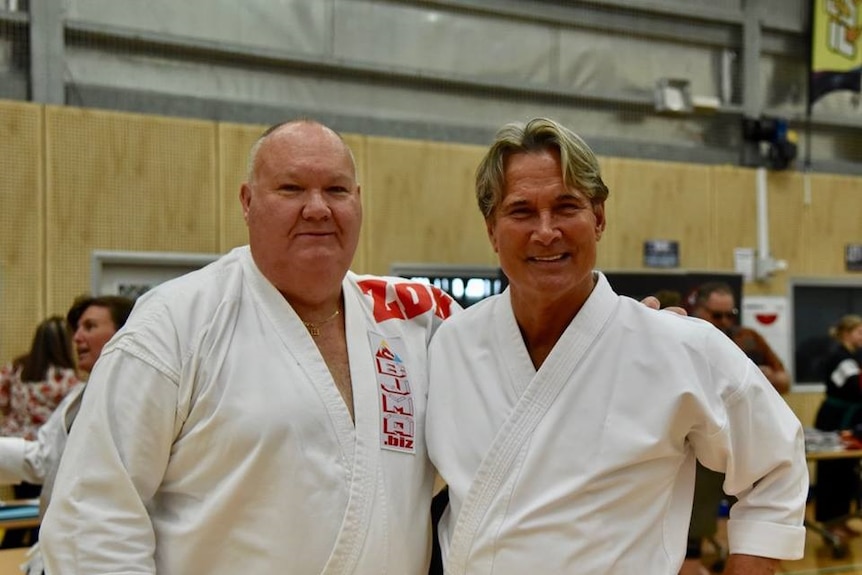 Two men standing in martial arts clothes smiling.