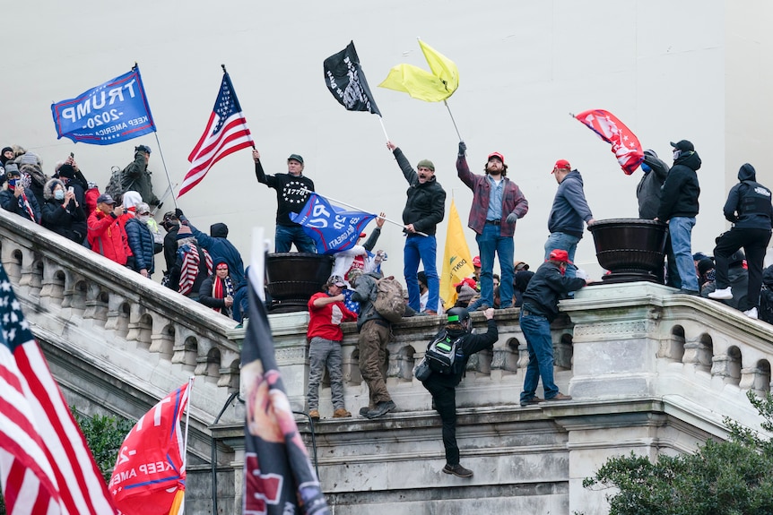 People stand on the US Capitol steps waving flags.