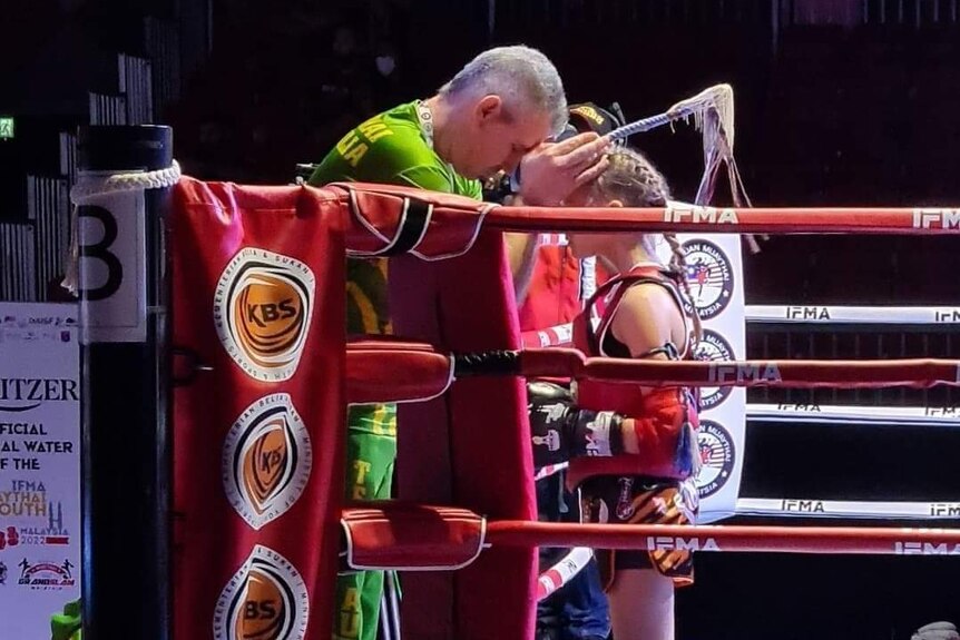 A coach and young girl stand inside a boxing ring