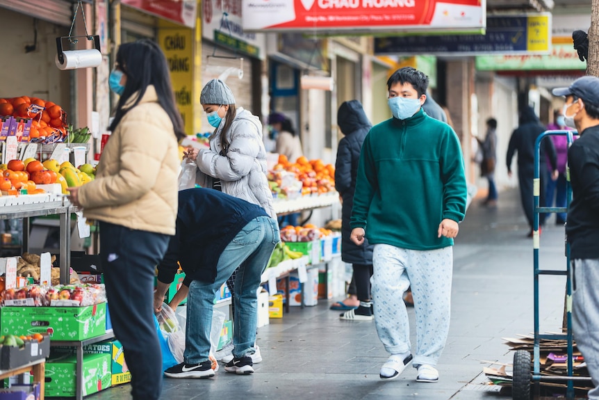 Shoppers wearing masks at the front of a fruit and vegetable shop. 