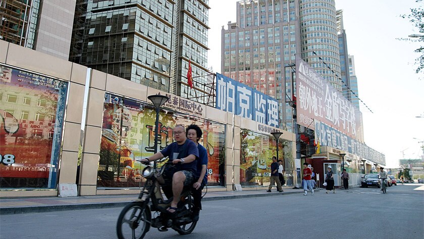 Two men ride a motorbike past a block of modern buildings in Beijing.