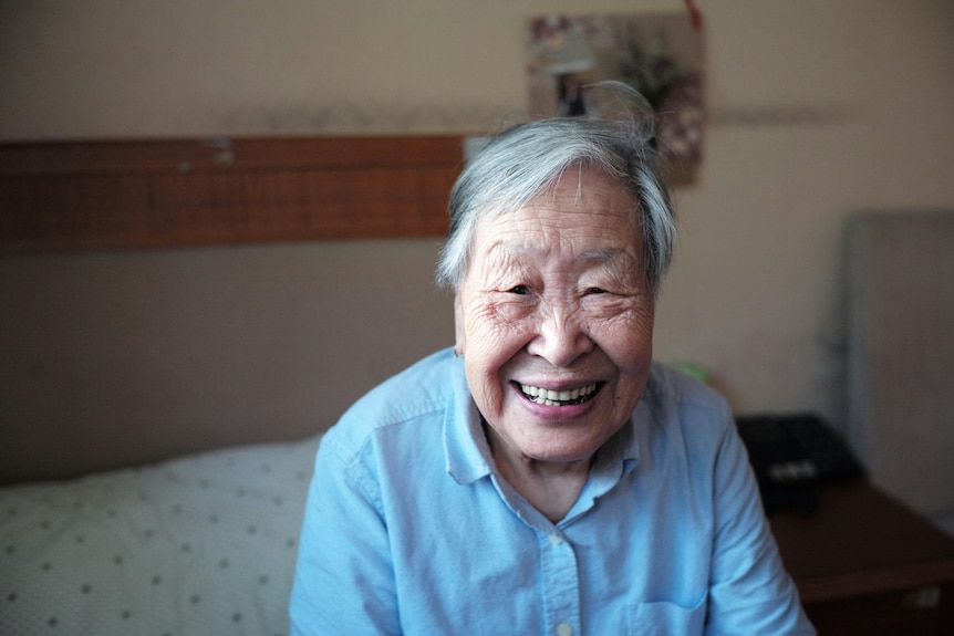 An elderly asian woman smiles at the camera 