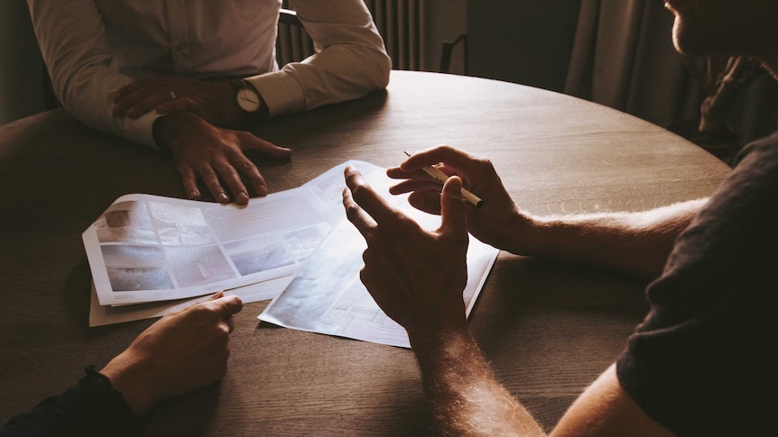 Three people sit at a table discussing a document for a story on unfair dismissal laws.