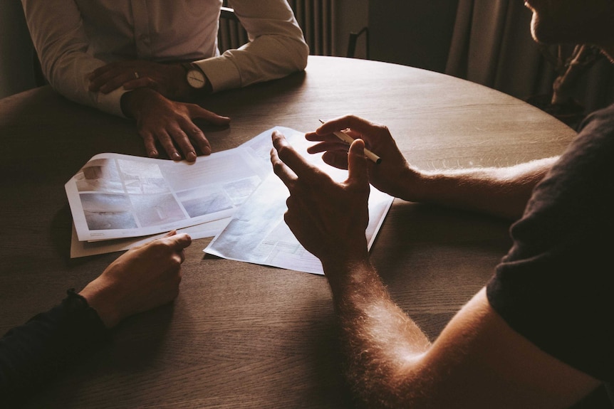 Three people sit at a table discussing a document for a story on unfair dismissal laws.