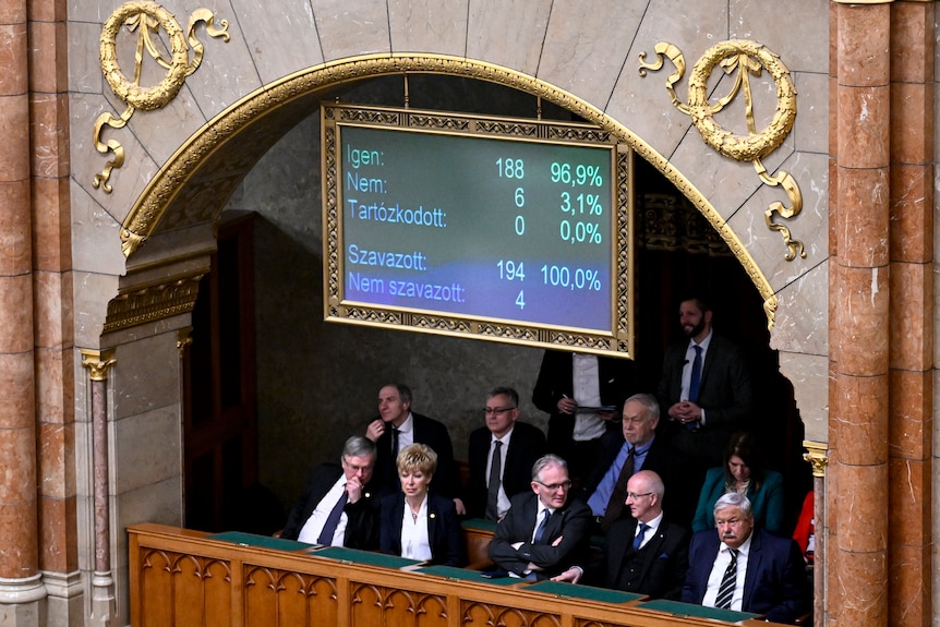 Image of Hungarian politicians sitting underneath a sign that counts the amount of votes for and against Sweden joining NATO.