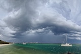 Storm clouds loom over a bay in which sailboats are anchored.