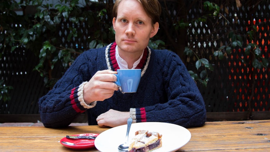 A man sits with a cup of coffee and a piece of cherry pie.