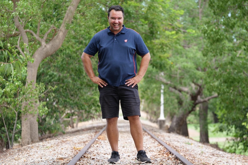Man standing on disused railway track laughing. Trees in background.