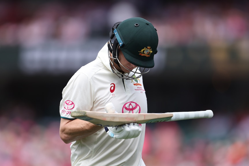 Steve Smith looks down while carrying his bat in one hand