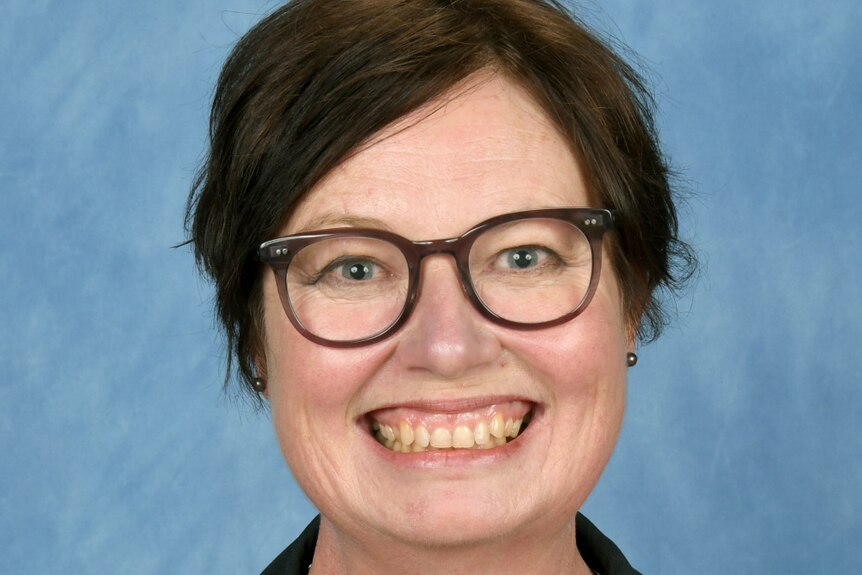 A woman with short brown hair and spectacles smiles