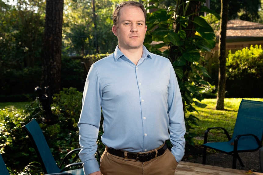 A man in a shirt and slacks stands in a backyard