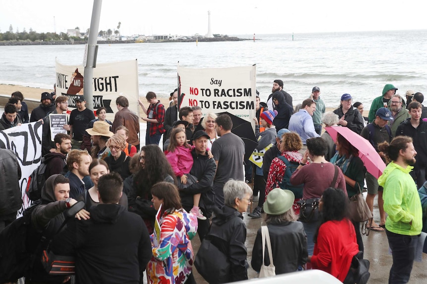 A group gathers with signs saying 'No to Racism, No to Facism'