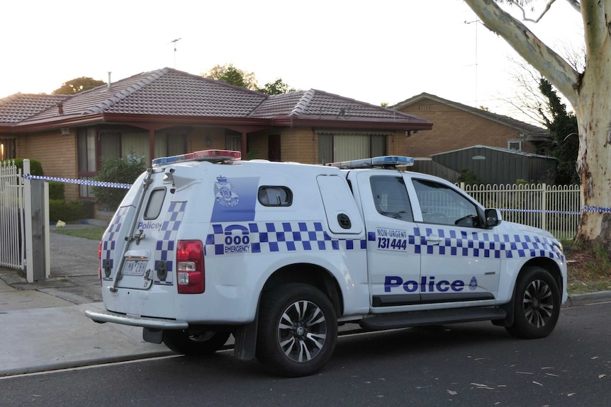 A police car parked outside a suburban house, which has police tape across its entrance.