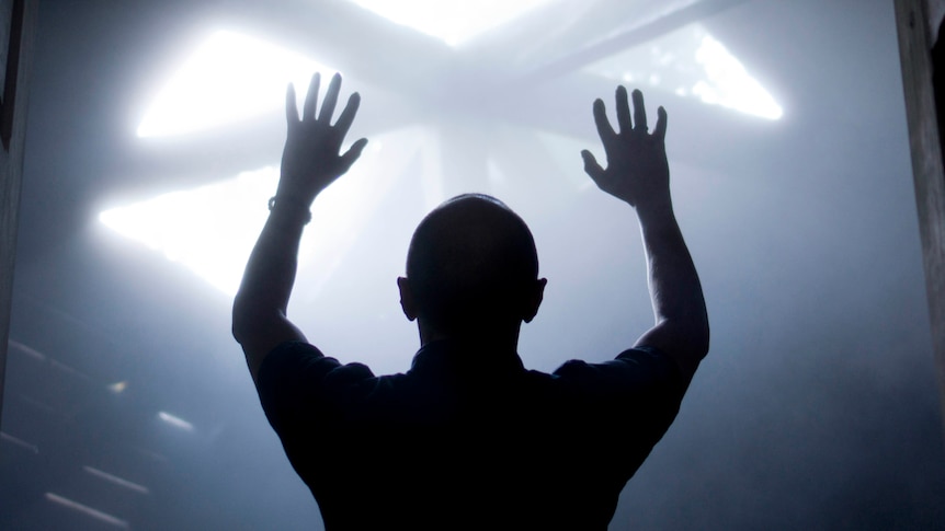 A man's silhouette with raised hands faces the light coming from above.